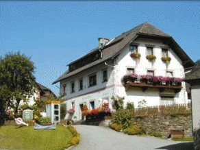 Das Gästehaus Moser: weißes Bauernhaus mit dunklen Holzbalkonen, Blumenkästen und Garten
